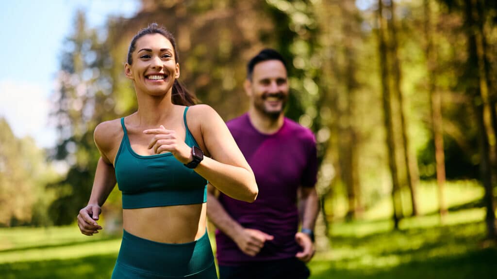 o femeie si un barbat practica sport, alearga in natura, fericiti