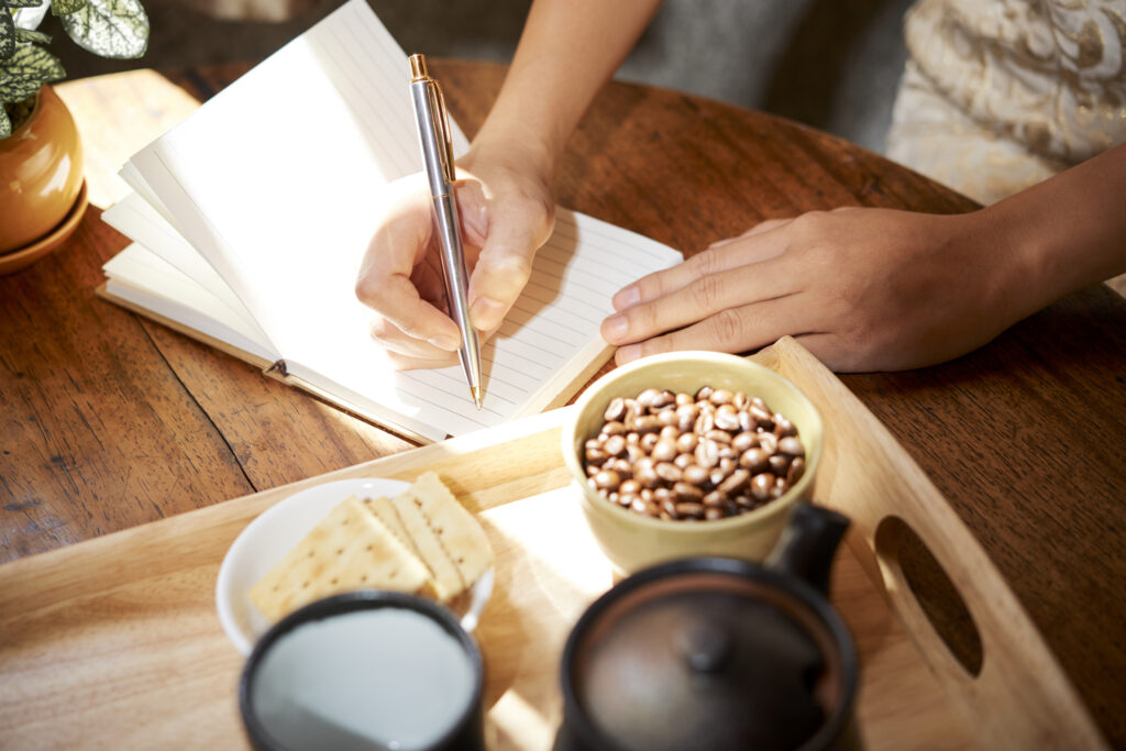 femeie care scrie în jurnalul alimentar pe masă de lemn, care are alături cafea și biscuiți