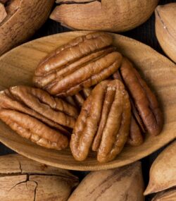Imagine de aproape cu o lingură de lemn cu miezul unor nuci pecan, pe un fundal de nuci pecan intregi